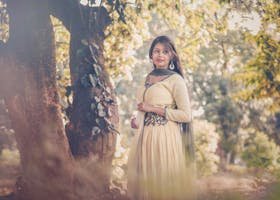 Portrait of a woman in traditional South Asian attire standing outdoors under trees.