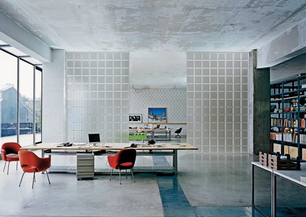 Contemporary office interior featuring tall partitions made of transparent glass bricks, creating open yet private workspaces.