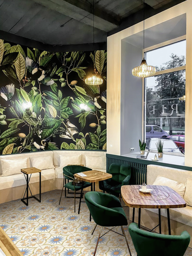 Modern cafe interior with green chairs and floral wall design featuring elegant tile colour combinations on the floor.