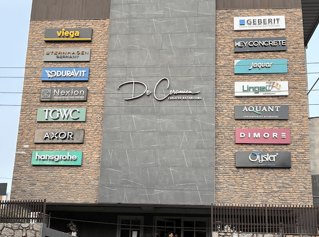 Exterior view of the De Ceramica showroom featuring branded signage from luxury bathroom and tile brands, modern stone façade design, and entrance steps.”