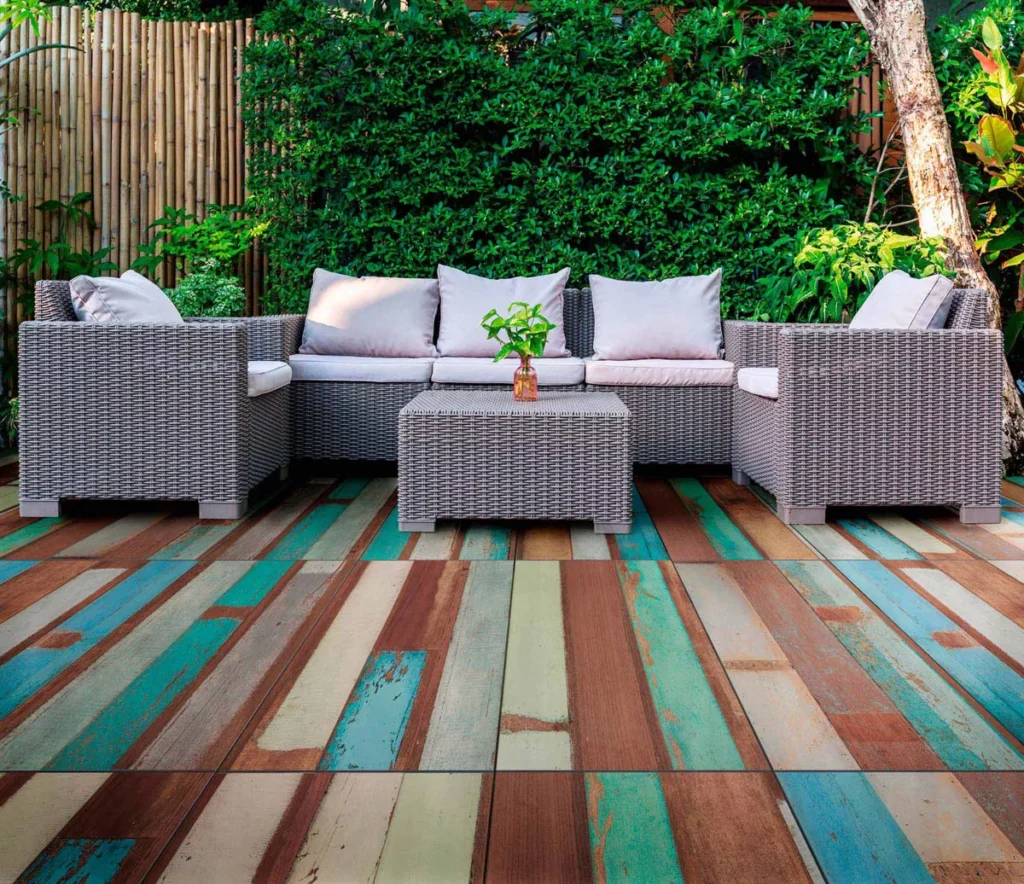 Colorful rustic wood-effect terrace tiles enhancing an outdoor seating area with wicker furniture and lush greenery.
