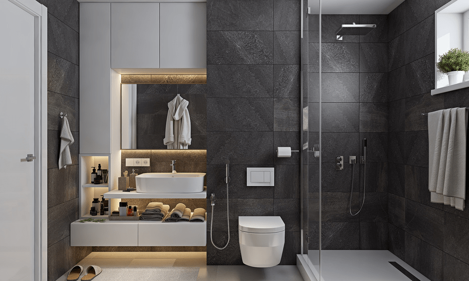 Contemporary luxury bathroom with wall hung toilet, concealed flush system, glass shower partition and textured dark tiles, reflecting how toilet position as per vastu can align with modern interior design in Gurgaon apartments.